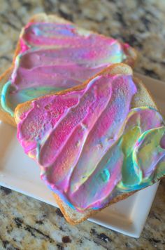 two pieces of bread with pink and blue icing on them sitting on a white plate