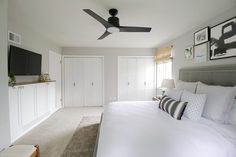 a bedroom with a ceiling fan and white bedding, along with pictures on the wall