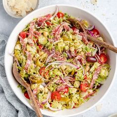 a white bowl filled with salad and wooden spoons next to some other food items