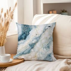 a blue and white pillow sitting on top of a couch next to a cup filled with coffee