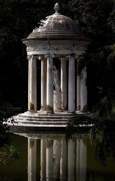 a statue in the middle of a pond surrounded by trees