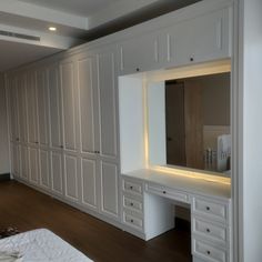 an empty bedroom with white cabinets and lights on the dressers, along with a large mirror