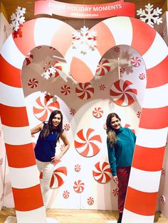 two women are standing in front of giant candy canes at the holiday moments booth