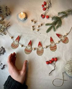 a hand holding a string of christmas decorations on a table with candles and other items