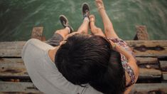 a man and woman laying on top of each other next to the ocean with their feet in the water