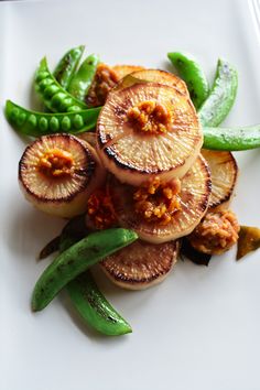 a white plate topped with sliced up vegetables and green beans next to pea pod pods