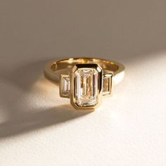 a yellow gold ring with three baguettes set in the middle, on a white surface