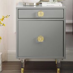 a gray and gold nightstand with flowers on it next to a white vase filled with yellow flowers