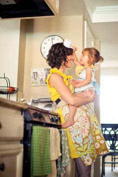 a woman holding a baby in her arms while standing next to a stove top oven