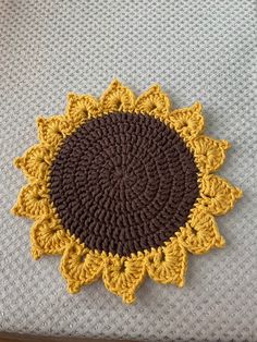 a crocheted sunflower sitting on top of a white bed sheet with brown and yellow trim