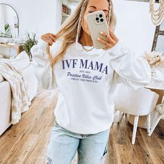 a woman taking a selfie while wearing a white sweatshirt with the words ivf mama printed on it