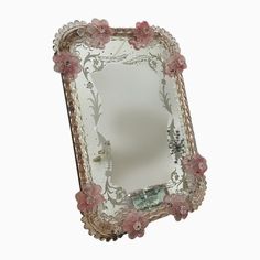 an ornately decorated mirror with pink flowers on the edges, against a white background