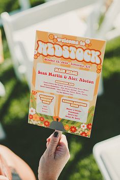 a person holding up a flyer for an outdoor wedding reception in the grass with chairs and tables behind them