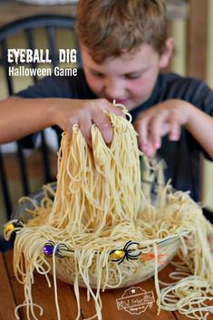 a young boy is eating noodles from a bowl on a table with the words eyeball dig halloween game