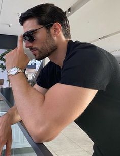 a man in sunglasses leaning on a railing with his hand to his face and looking off into the distance