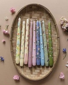 a wicker tray with seven candles in different colors and designs on it next to flowers