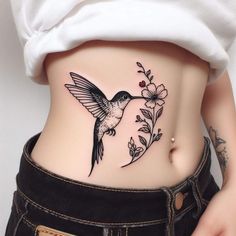 a woman's stomach with a hummingbird and flower tattoo on her lower side