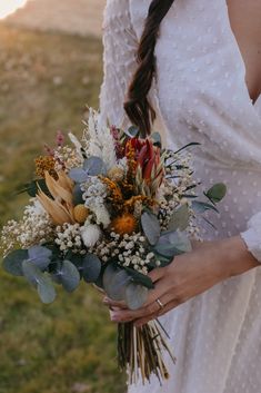 a woman in a white dress holding a bouquet of wildflowers and greenery