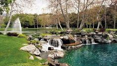 there is a small waterfall in the middle of this park with green grass and trees