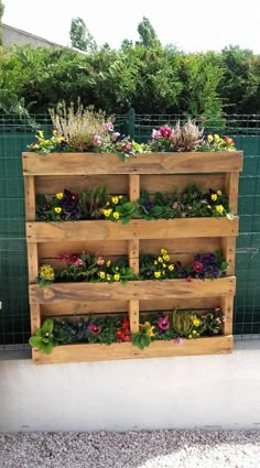 a wooden planter filled with lots of flowers next to a green fence and bushes