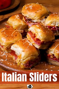 small sandwiches with meat and cheese are piled on a wooden platter that says italian sliders