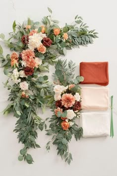 an arrangement of flowers and greenery laid out on a white surface next to each other