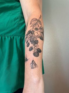 a woman's arm with flowers and butterflies tattooed on her left arm, in front of a gray wall