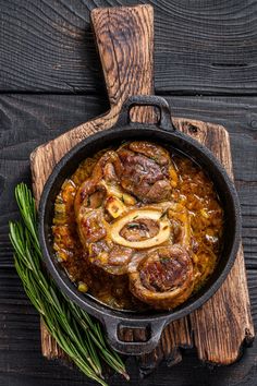 a skillet filled with meat and onions on top of a wooden cutting board