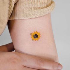 a small sunflower tattoo on the side of a woman's right arm