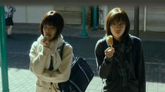 two young women standing next to each other on a brick walkway, one eating an ice cream cone