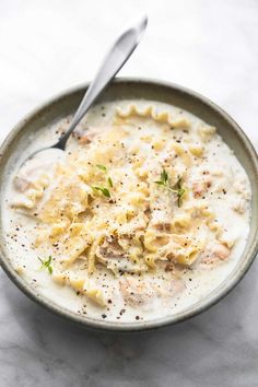 a bowl filled with pasta and sauce on top of a marble counter next to a spoon