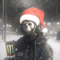 a man wearing a santa hat sitting in the snow with a skull on his face