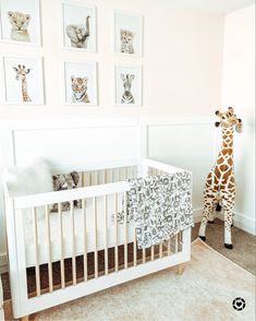 a giraffe standing next to a baby crib in a room with pictures on the wall