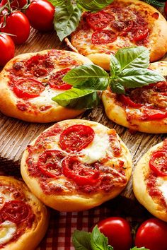 several small pizzas on a table with tomatoes and basil leaves around them, ready to be eaten