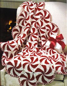 a red and white crocheted blanket with a bow on it next to a fireplace