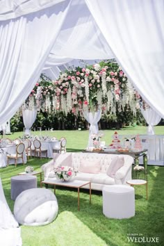 an outdoor wedding setup with white drapes and pink flowers on the top of it