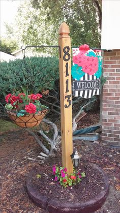 a welcome sign in front of a tree and some flowers on the ground near a brick building