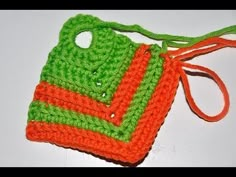 an orange and green crocheted bag with a tag attached to the handle on a white surface