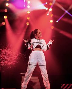 a woman standing on top of a stage in front of red and purple lights with her arms out