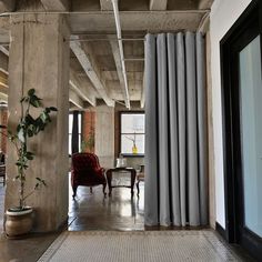 an empty room with a red chair and large window covered in grey drapes next to a potted plant