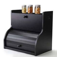 three jars are sitting on top of a black shelf that is holding food and spices