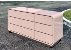 a pink dresser sitting on top of a parking lot next to a green planter