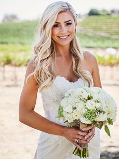 a beautiful blonde woman in a wedding dress holding a bouquet of white and green flowers