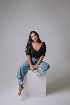 a woman sitting on top of a white box wearing ripped jeans and a black shirt