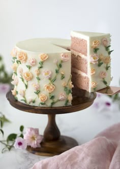 a white cake with pink and yellow flowers on it, sitting on a wooden stand