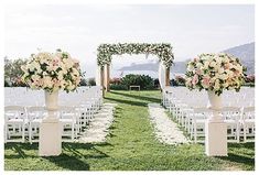 an outdoor ceremony setup with white chairs and flowers in vases at the end of the aisle