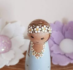 a small wooden doll sitting on top of a table next to white and purple flowers