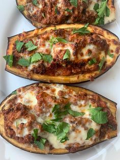 three stuffed eggplant boats on a white plate with parsley and basil garnish