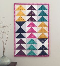 a colorful quilt hanging on the wall next to a vase