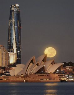 the full moon is setting over sydney, australia's opera house and skyscrapers